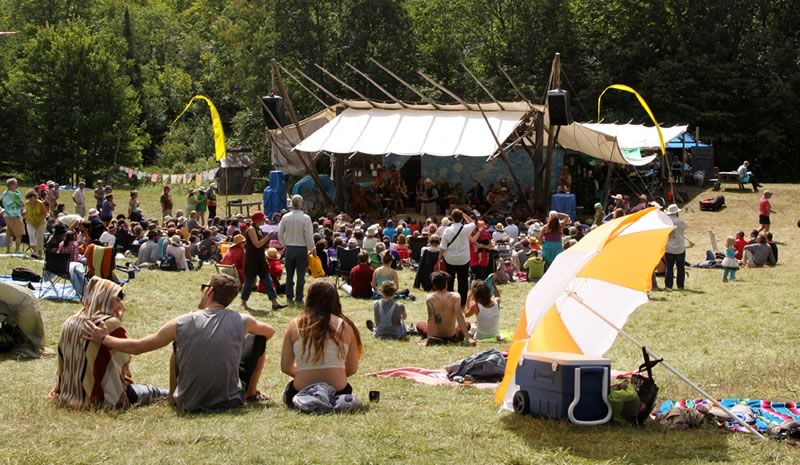 Photo of folks sitting on the hill watching a performance on the main stage at Blue Skies